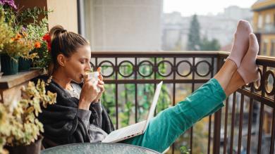 
		A young woman sits relaxed on the balcony and works
	